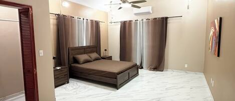 Une chambre à coucher avec un lit, des rideaux, un ventilateur de plafond et un luminaire.