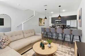 A modern living room with a sofa, coffee table, and a dining area with bar stools. - COZY & Modern Townhome w/ Themed Room | Near Disney (3237) (Kissimmee)