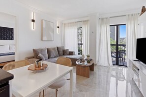 Ein modernes Wohnzimmer mit einer Couch, einem Esstisch, einem Fernseher und einem Balkon mit Vorhängen.