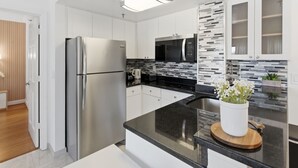 A modern kitchen with white cabinets, stainless steel appliances, and a black countertop. - NEW Cozy Apt | Near Universal, Icon Park & IDrive (6165-1304) (Orlando)