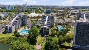 A high-rise building with a swimming pool, surrounded by greenery and other buildings. - NEW Cozy Apt | Near Universal, Icon Park & IDrive (6165-1304) (Orlando)
