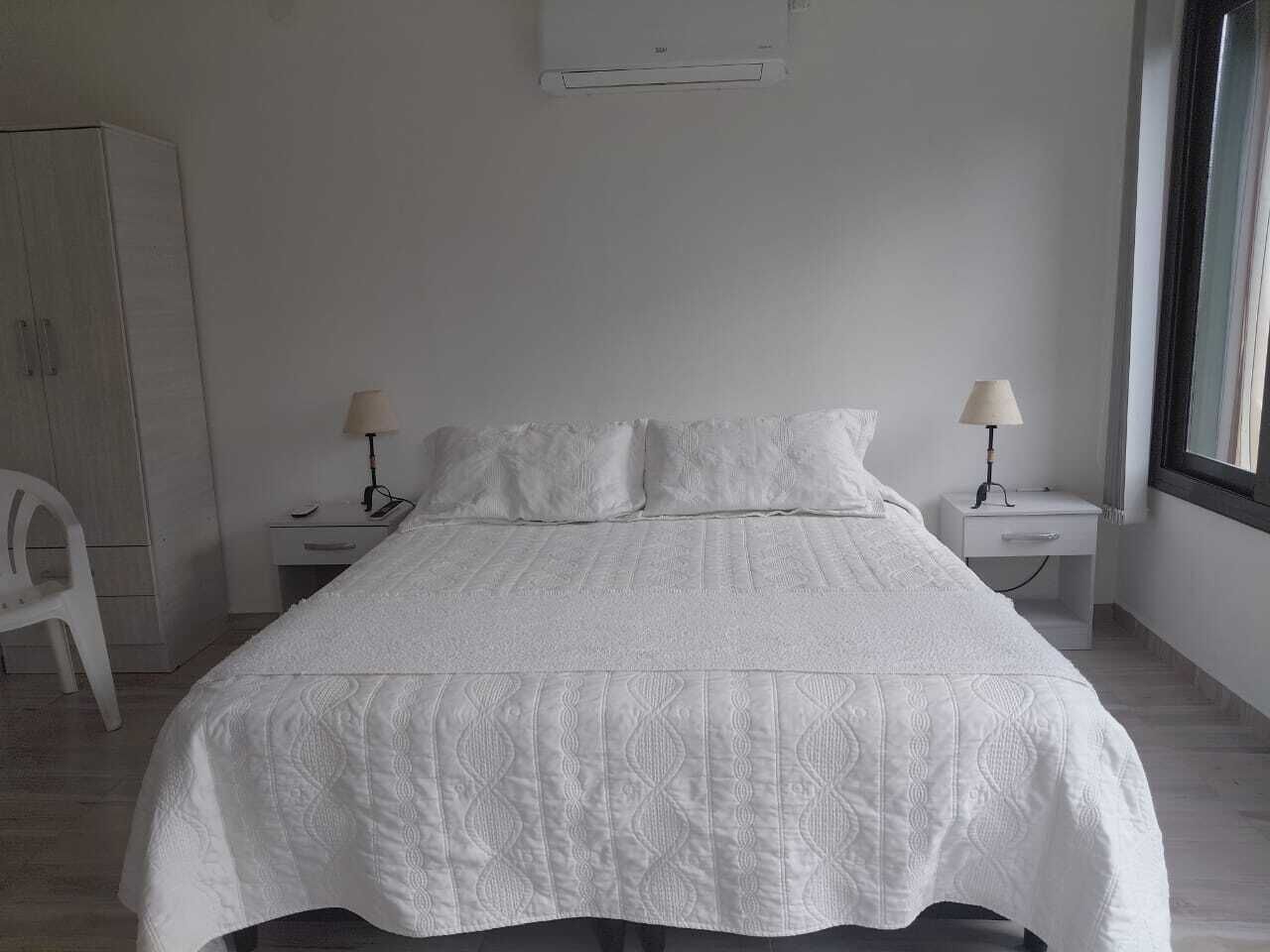 A bedroom with a bed, two bedside tables, a chair, and a window.