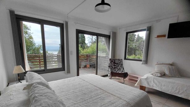 Une chambre avec un grand lit, deux petits lits, une chaise et un balcon avec vue.