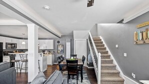 Eine moderne Küche mit weißen Schränken, ein Essbereich mit Tisch und Stühlen sowie eine Treppe zu einer weiteren Ebene.