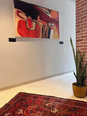 A hallway with a large abstract painting, a patterned rug, and a potted plant. - Studio L 2 min from the corniche and ain diab (Casablanca)