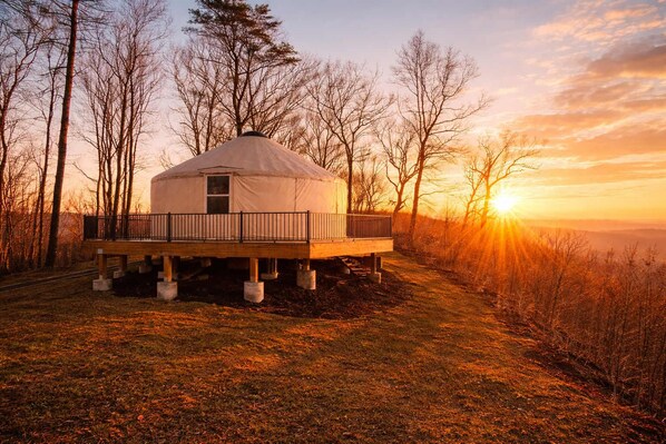 Ein Jurte mit einer Holzterrasse, umgeben von Bäumen, während der Sonnenuntergang stattfindet.