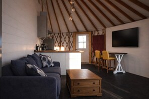 Ein gemütliches Wohnzimmer mit Sofa, Couchtisch und Fernseher. Es gibt eine Küchenzeile mit Fenster und einem Esstisch mit Stühlen.