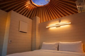 A room with a sloped ceiling, a skylight, a bed with white bedding, and a wall-mounted air conditioning unit. - Cozy Mountaintop Glamping Yurt w/Kitchen and Bath (Rising Fawn)