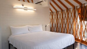 Ein Schlafzimmer mit Bett, weißen Wänden, Holzbalken und einem Fenster mit Gitterstruktur.