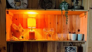 Interior de madera con un reloj, una lámpara y estantes con platos, vasos y una tetera.
