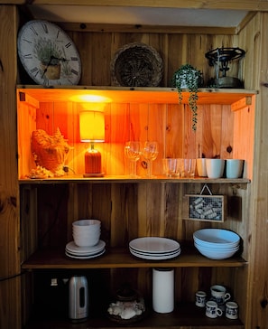 Ein Holzinterieur mit einer Uhr, einer Lampe und Regalen mit Tellern, Gläsern und einem Wasserkocher.