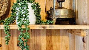 Una estantería de madera con un jarrón blanco, plantas verdes, un farol de latón y varios vasos de cristal.