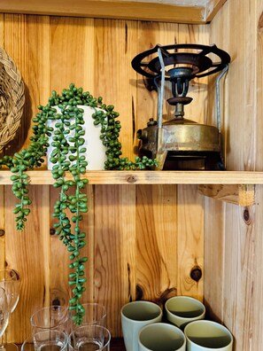 A wooden shelf with a white vase, green plants, a brass lantern, and several clear glasses. - Fisherman's Cave (Faro)