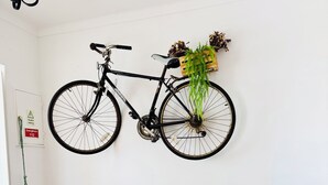Un sofá verde, una bicicleta montada en la pared, una mesita con una lámpara y un letrero de emergencia también fijado a la pared.