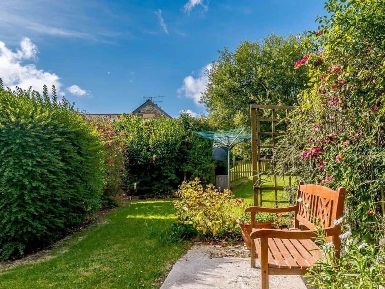 A garden with a bench, a wooden fence, and a house in the background.