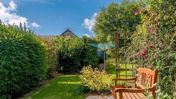A garden with a bench, a wooden fence, and a house in the background.