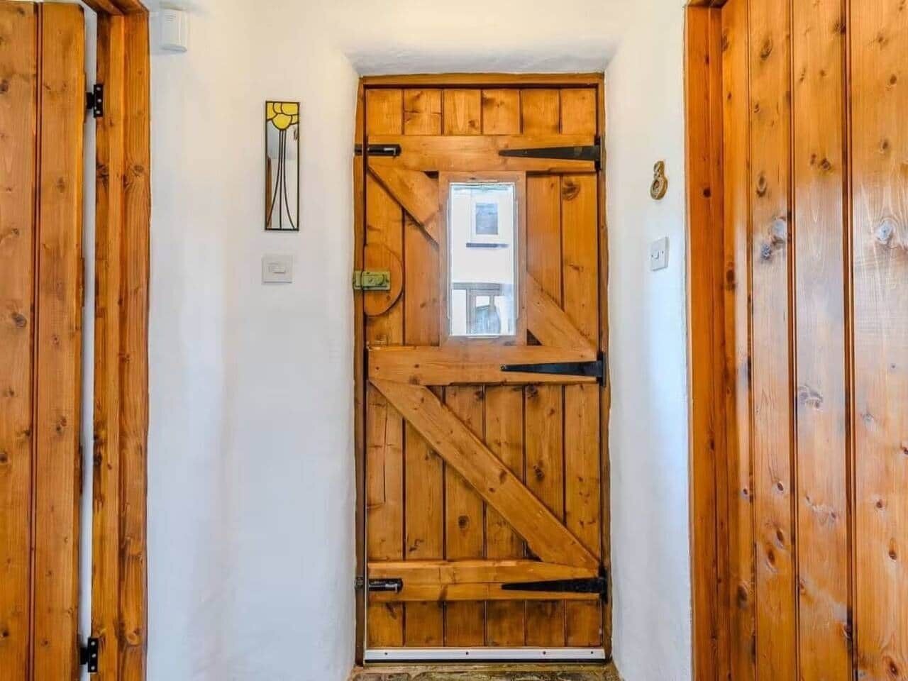 A wooden door with a window, a wall-mounted light switch, and a small picture frame.