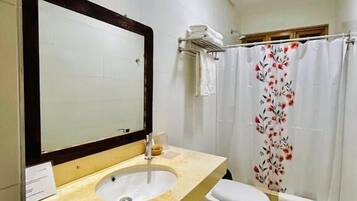 Un baño con lavabo, espejo, inodoro, cortina de ducha y toallero.