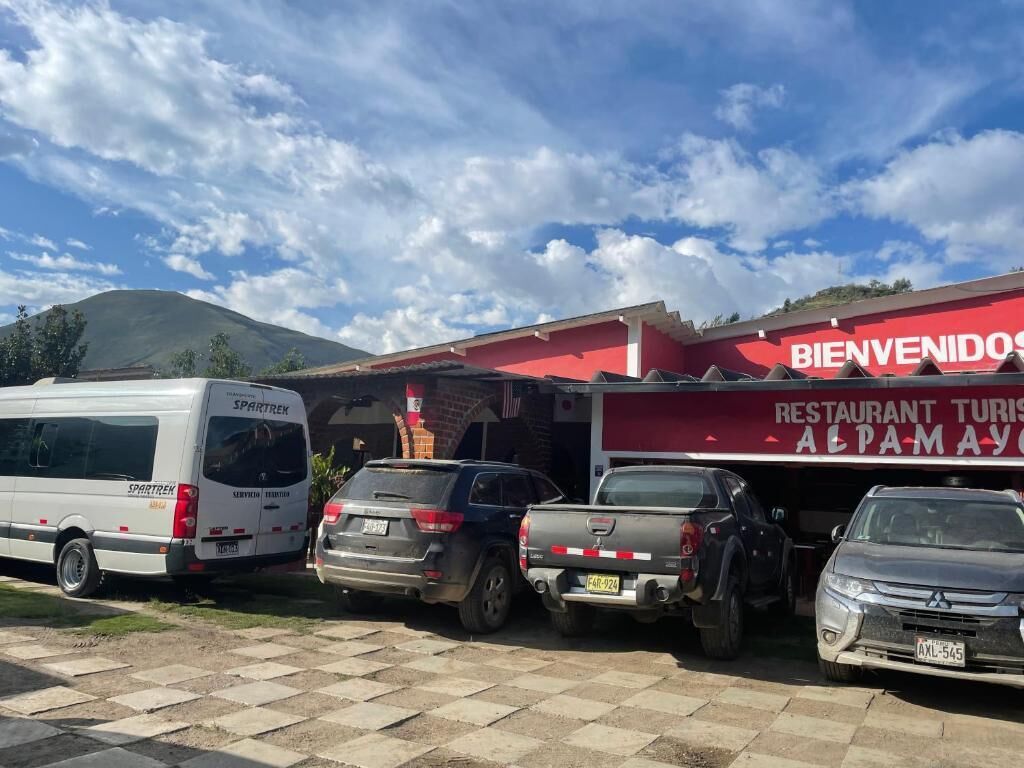 A parking lot with several vehicles, a building with a red awning, and a mountain in the background.