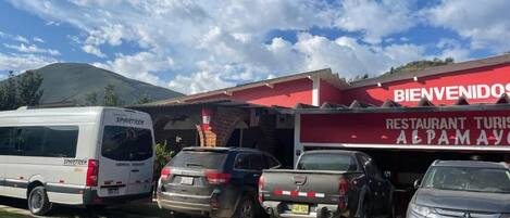 A parking lot with several vehicles, a building with a red awning, and a mountain in the background.