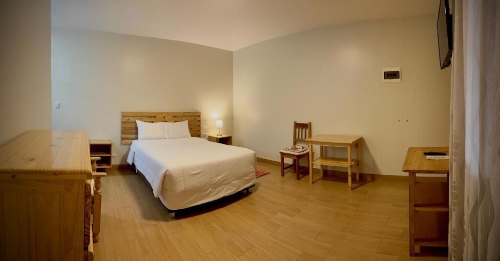 A bedroom with a bed, bedside table, chair, and desk.
