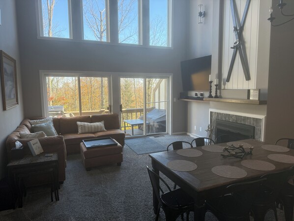 Una sala de estar amplia con un ventanal grande, una chimenea y un comedor con mesa preparada para cuatro.
