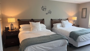 Habitación de hotel con dos camas, cada una con cabecero de madera, ropa de cama blanca y una manta verde. Hay lámparas de noche en cada mesita.