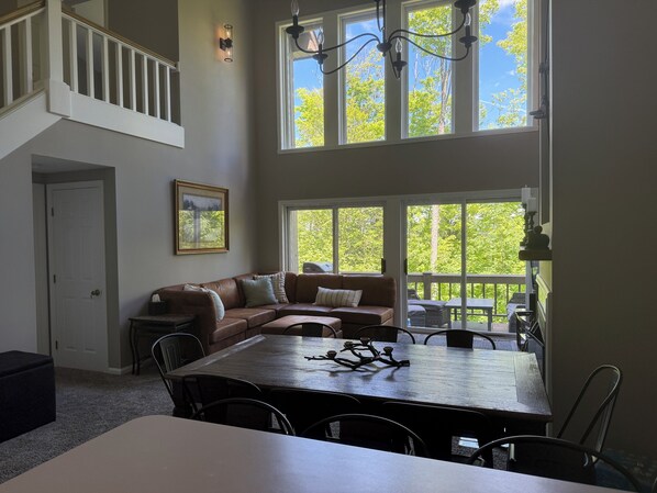 A spacious living area with a large dining table, a brown leather sofa, and a staircase leading to an upper level.