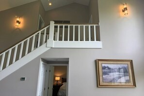 Una escalera con barandillas blancas que conduce a un nivel superior, un cuadro en la pared y una puerta que da a un dormitorio.