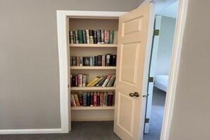Una habitación con una estantería que contiene varios libros y una puerta que da a otra estancia.
