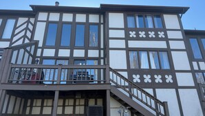Un edificio de dos plantas con balcón, escalera y una parrilla exterior visible.