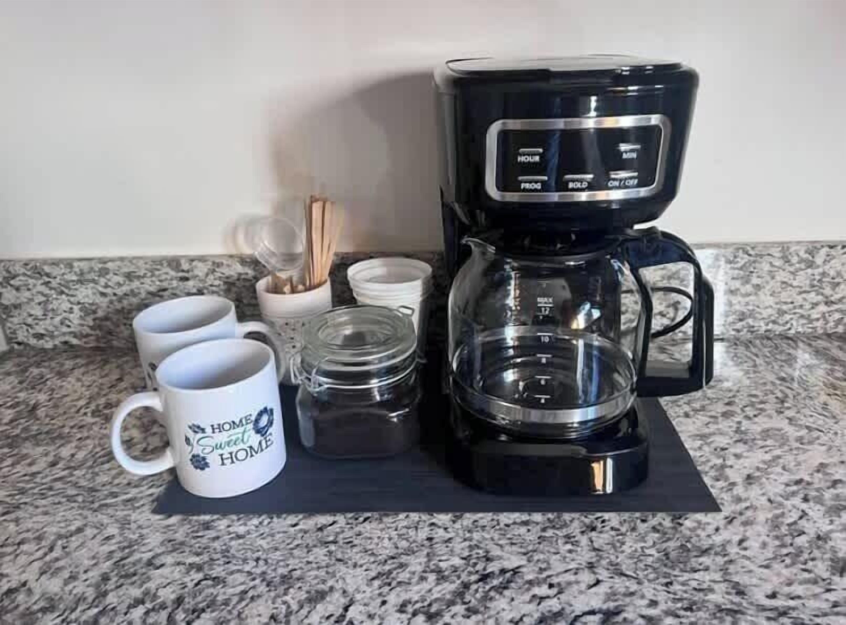 A kitchen counter with a coffee maker, two mugs, and a glass jar.