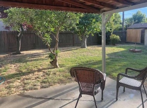 A covered patio with two wicker chairs, a wooden fence, and a grassy yard.
