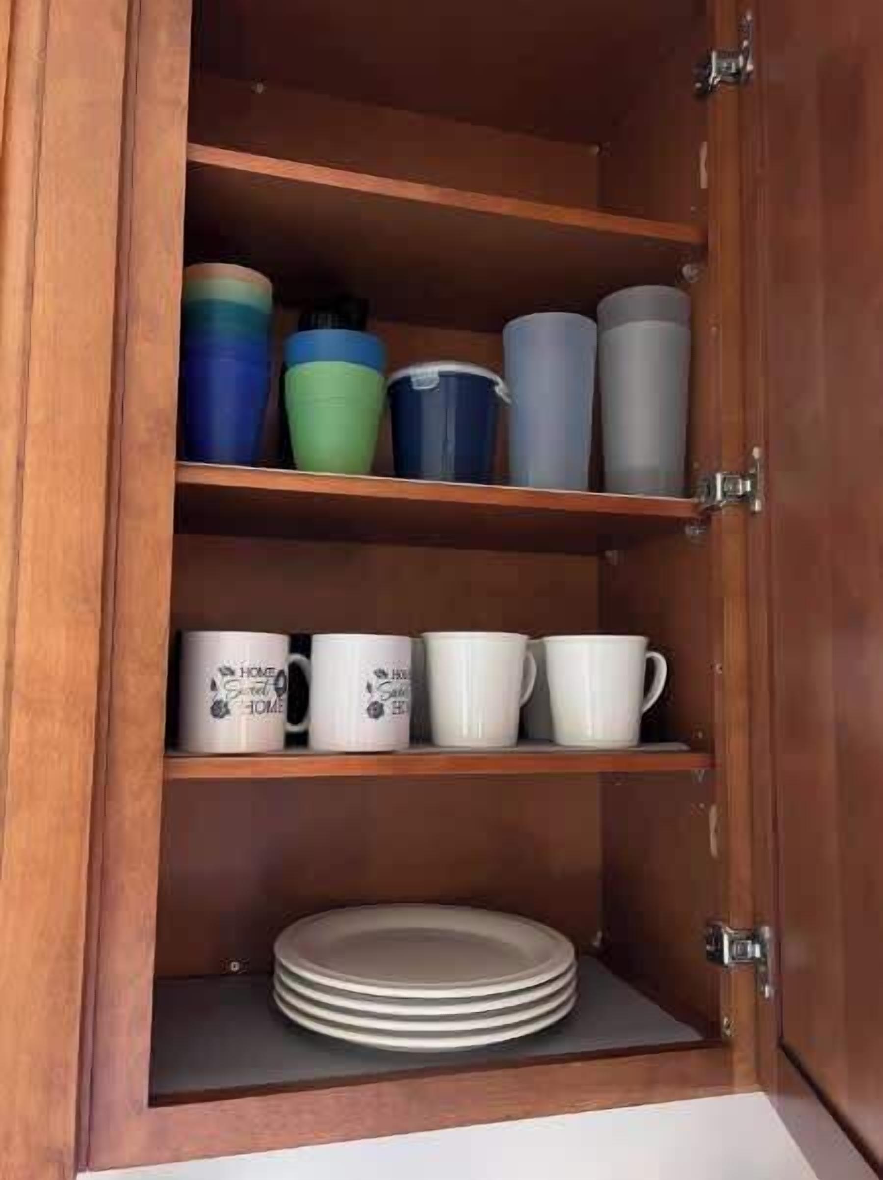 A wooden cabinet with shelves containing various mugs and a stack of plates.