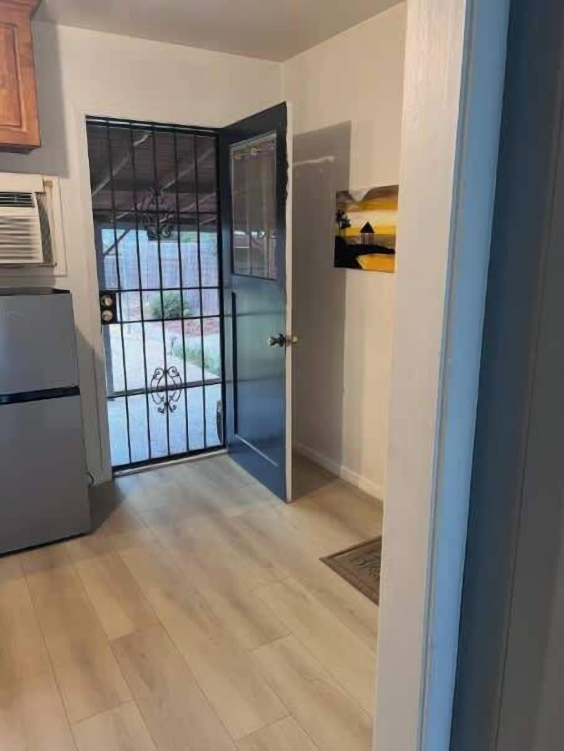 Eine Küche mit Kühlschrank, einer Tür mit Metallgitter und einem kleinen Regal mit einem Bild.