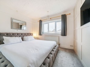 Ein Schlafzimmer mit einem großen Bett, einem Spiegel, einem Fenster mit Vorhängen und einer Heizung.