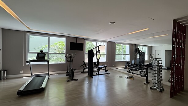 A spacious gym with a treadmill, weight machines, and a mirror wall. - Clementino 110 (São Paulo)
