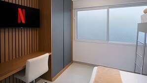 A modern hotel room with a large window, a TV mounted on a wooden panel, a white chair, and a bunk bed. - Clementino 110 (São Paulo)