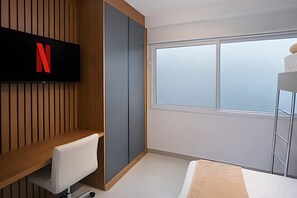 Una habitación de hotel moderna con un ventanal grande, un televisor montado en un panel de madera, una silla blanca y una cama litera.