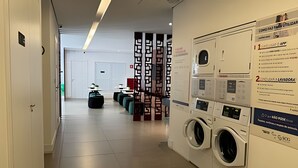 A hotel corridor with a washing machine, a seating area, and a door at the end. - Clementino 110 (São Paulo)