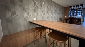 A modern bar area with a geometric wall design, wooden bar counter, and stools. - Clementino 110 (São Paulo)