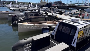 Marina con varios barcos amarrados, un bote inflable pequeño en primer plano y un cielo azul despejado.