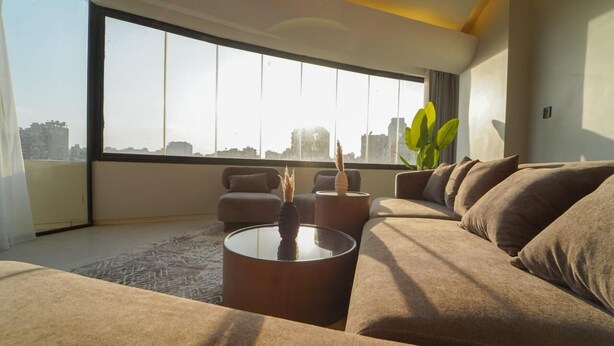 Een moderne woonkamer met een groot raam, een bank, een salontafel en een plant.