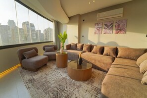 Ein modernes Wohnzimmer mit großem Fenster, einem Ecksofa, zwei Sesseln, einem Couchtisch und einer Zimmerpflanze.