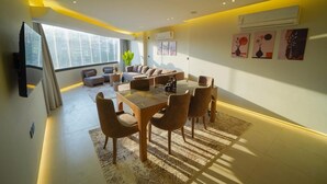 Een moderne woonkamer met een eethoek, grote ramen en kunstwerken aan de wanden.