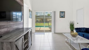 A spacious living area with a large sliding glass door leading to a pool, a dark blue sofa, a marble coffee table, and a wooden cabinet. - Disney & Universal Escape 4 Bedroom Private Pool Orlando Theme Parks (Kissimmee)