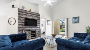 A modern living room with a fireplace, a flat-screen TV, and blue sofas. - Disney & Universal Escape 4 Bedroom Private Pool Orlando Theme Parks (Kissimmee)