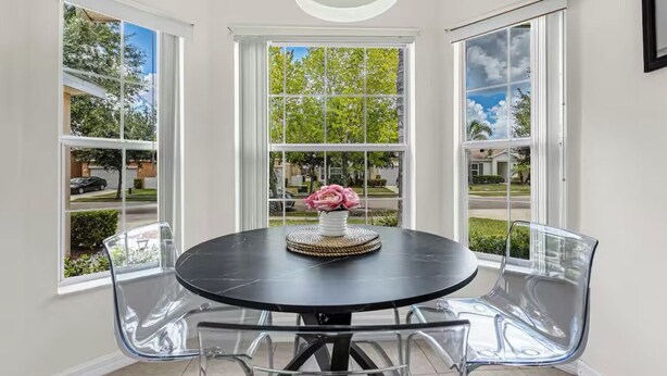 A corner room with a round table, clear chairs, and large windows with a view of a residential area. - Disney & Universal Escape 4 Bedroom Private Pool Orlando Theme Parks (Kissimmee)