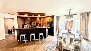 A modern kitchen with wooden cabinets, a central island with stools, and a dining area with a table and chairs.