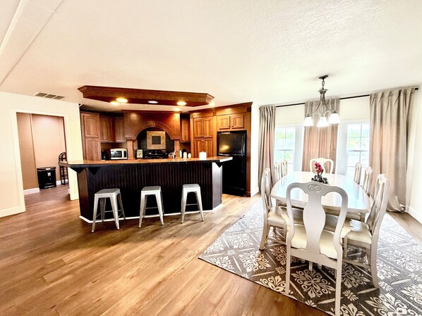 A modern kitchen with wooden cabinets, a central island with stools, and a dining area with a table and chairs.
